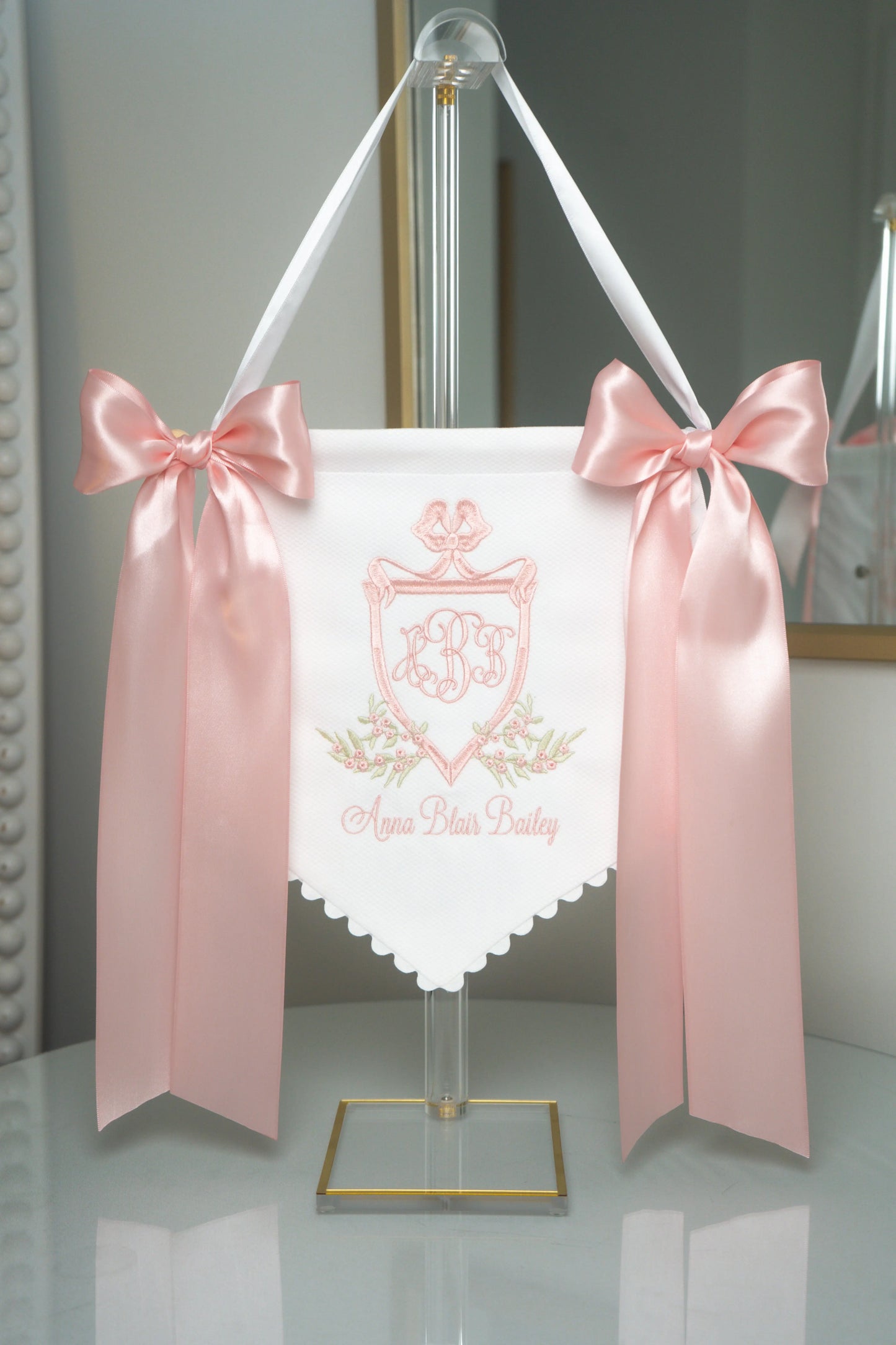 Personalized victorian baby banner with embroidered monogram and ribbon bows for nursery display; styled view