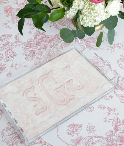 Pink toile monogram acrylic tray styled on a floral surface with green leaves