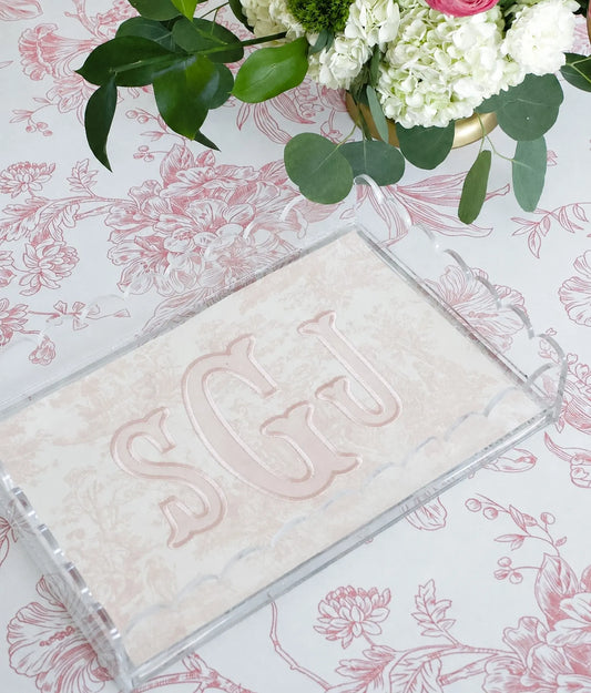 Pink toile monogram acrylic tray styled on a floral surface with green leaves