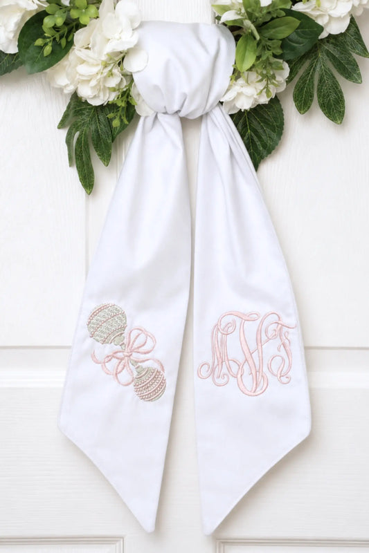 Personalized baby rattle wreath sash with embroidered motif for a decorative front door wreath; styled view