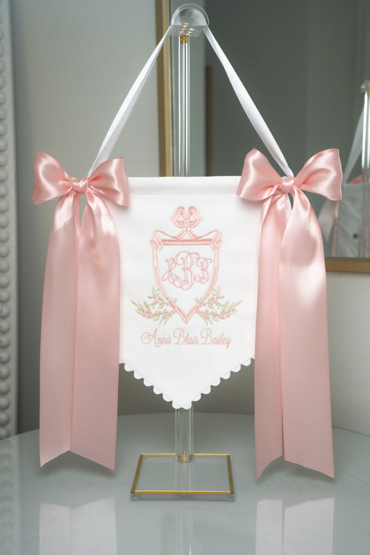 Personalized victorian baby banner with embroidered monogram and ribbon bows for nursery display; styled view