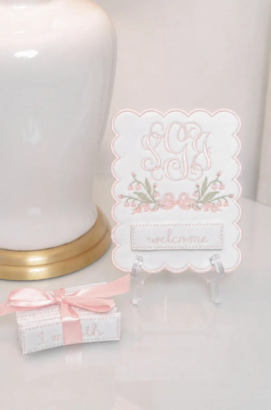 White scalloped baby milestone plaque with pink monogram, bell flower accents, and interchangeable welcome card